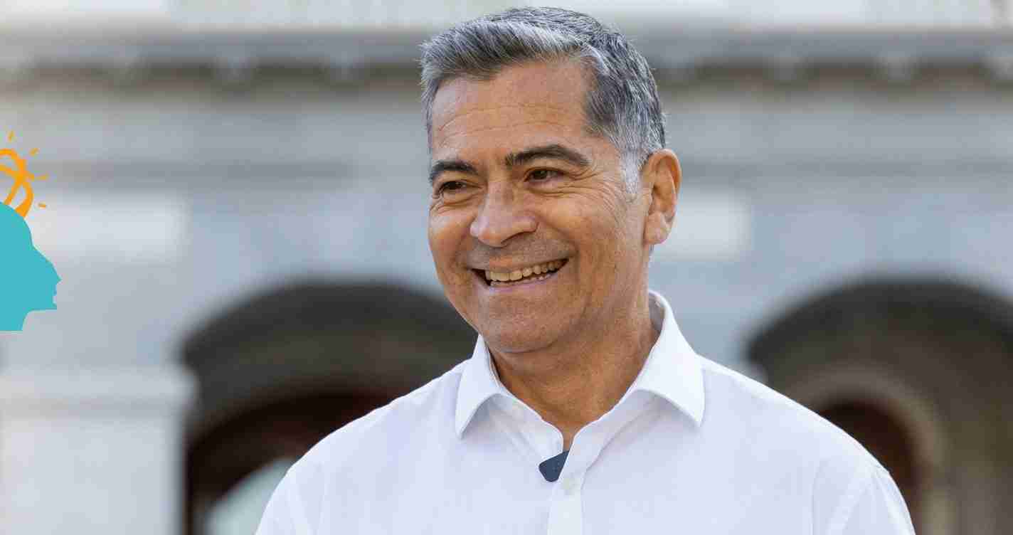 Smiling man in a white shirt wearing a lavalier microphone outdoors, photographed in a candid moment.