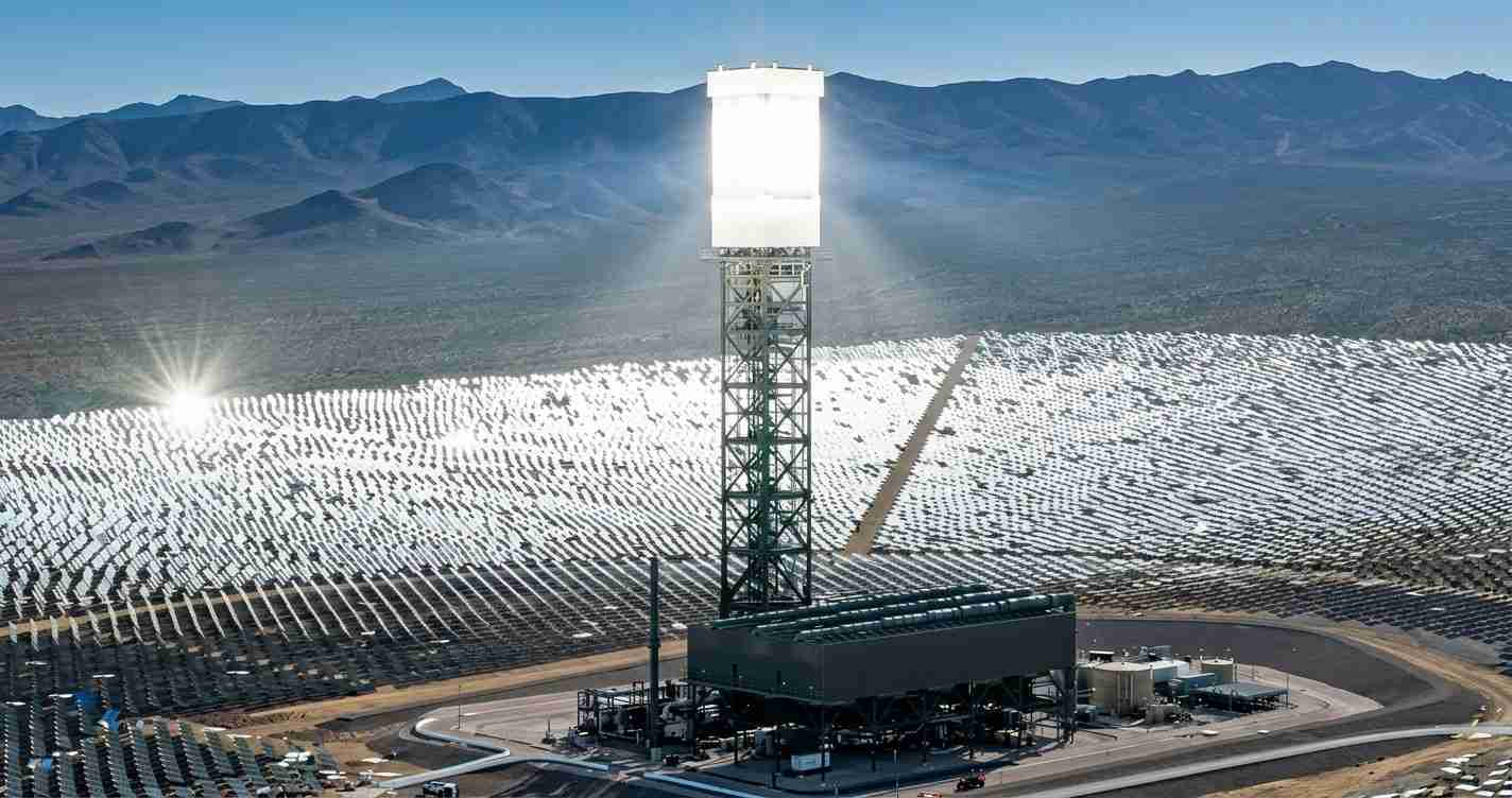 Solar power plant with a tall heliostat tower and a field of mirrors stretching across a desert landscape at dusk/dawn light.