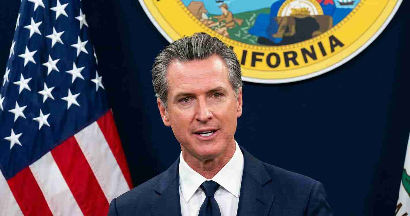 Politician in a navy suit giving a speech, with the California seal and U.S. flag behind.