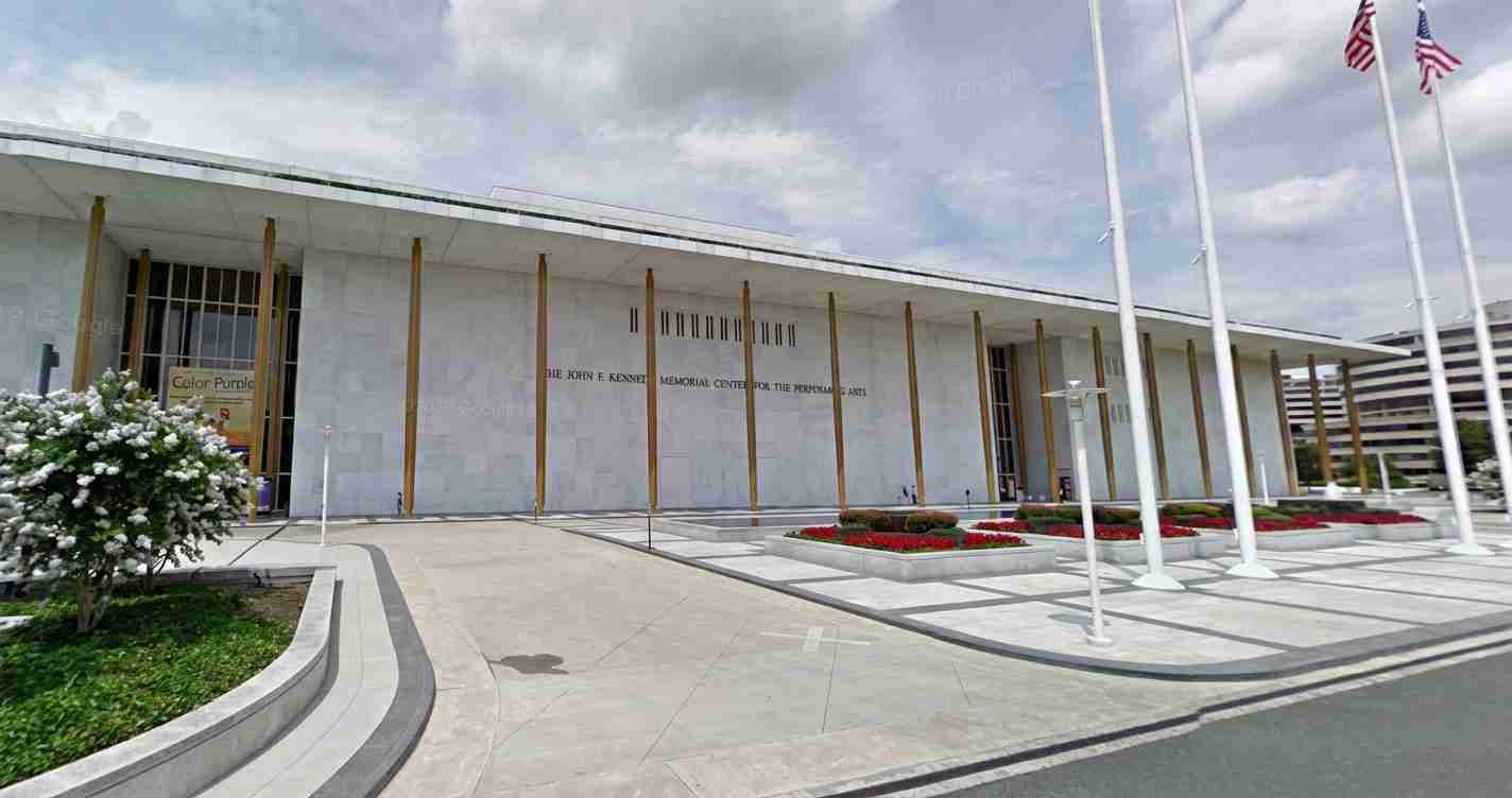 Modern memorial center or cultural arts building with tall gold pillars, flagpoles, and a landscaped plaza in front.