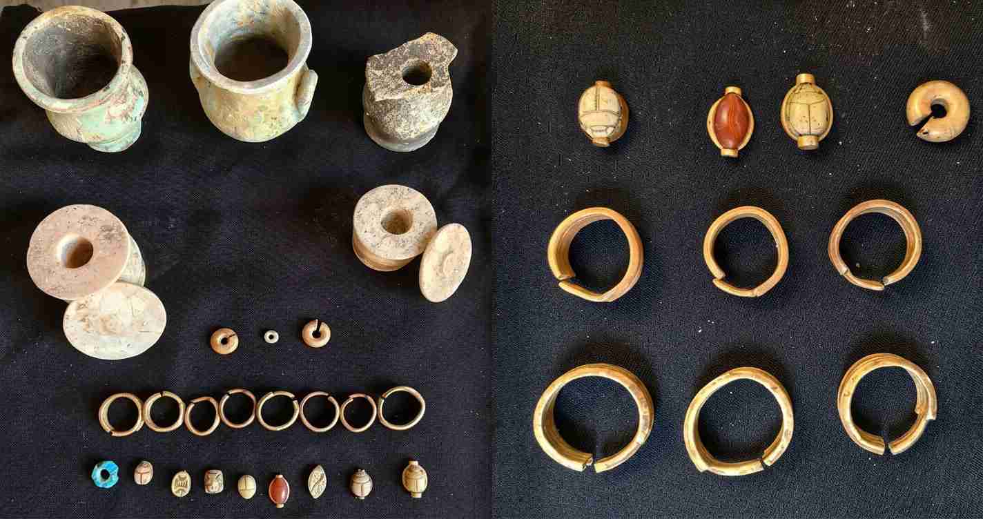 Ancient jewelry and beads laid out on a black surface, including rings, bangles, and carved beads with clay vessels on the left.