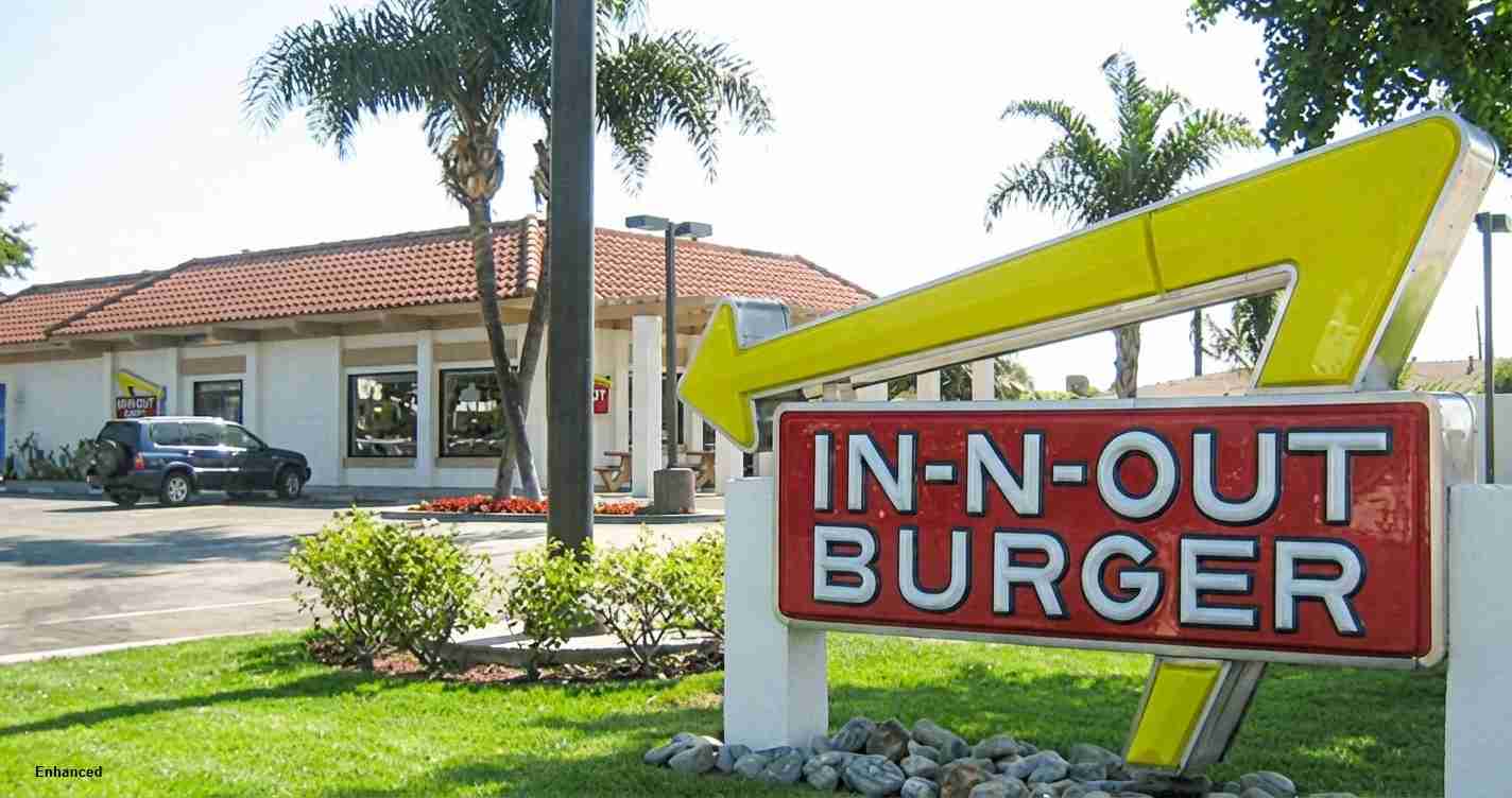 In-N-Out Burger sign with a large yellow arrow exterior of a fast-food restaurant under palm trees.