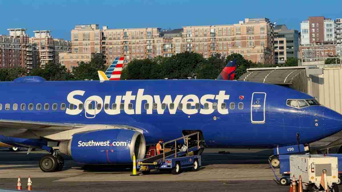 Southwest Airlines jet at gate with boarding ramp and ground crew nearby on tarmac.