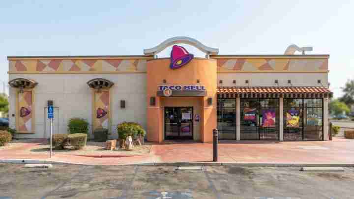 Taco Bell fast-food restaurant exterior with orange entrance and purple bell logo on a curved facade.