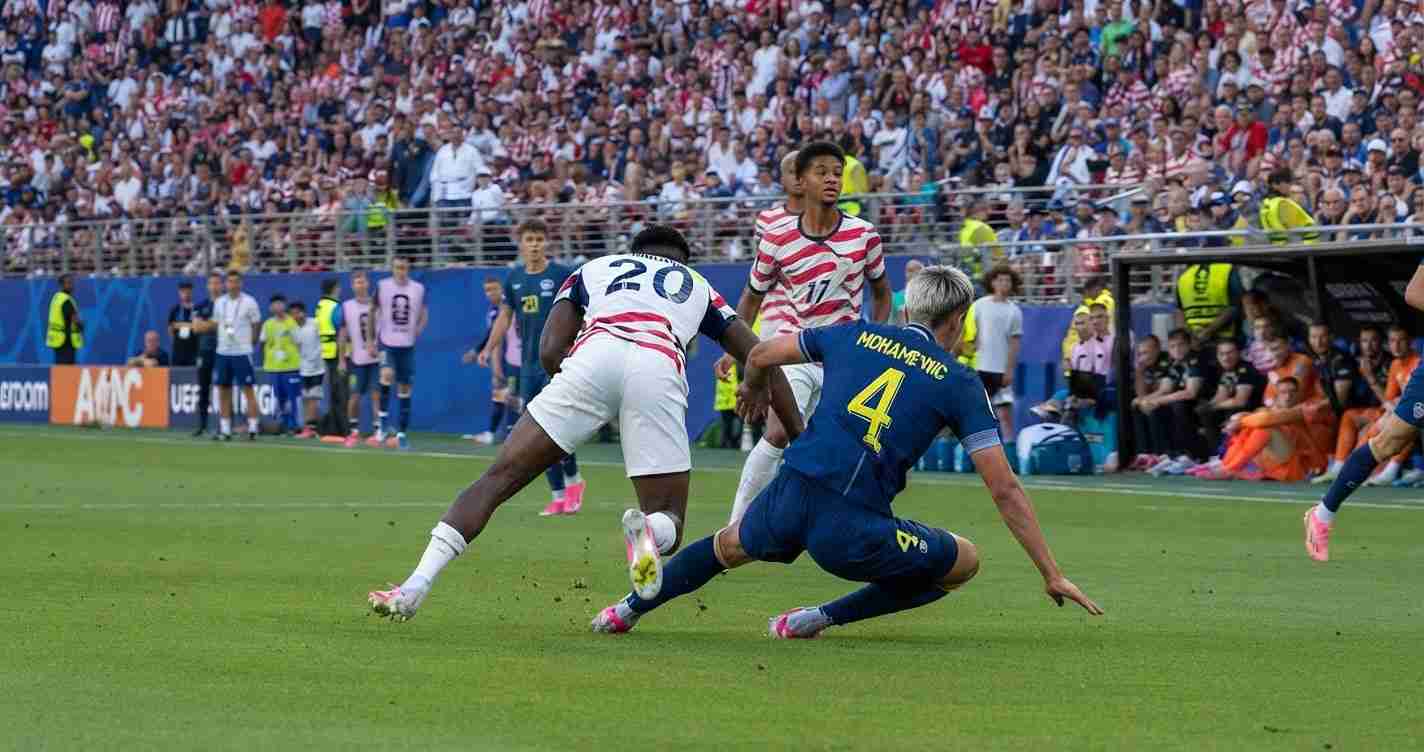 Soccer match: a player in white-and-red stripes and a blue kit compete for the ball as a sliding tackle unfolds on the field with a packed stadium in the background.